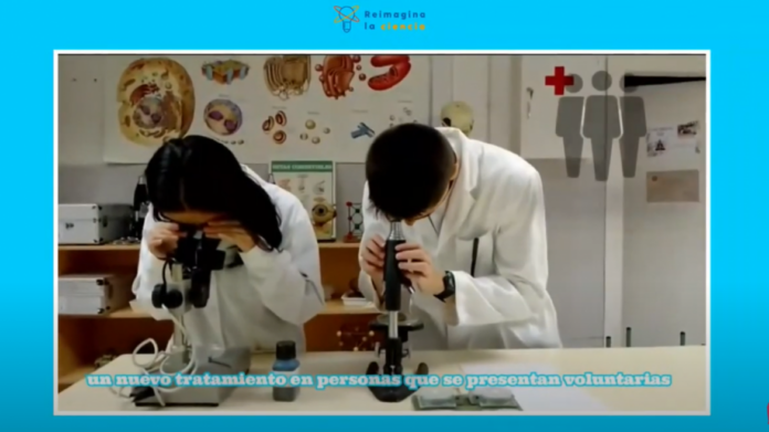 imagen en una pantalla de un plan de un vídeo donde dos alumnos con bata miran a través de un microscopio