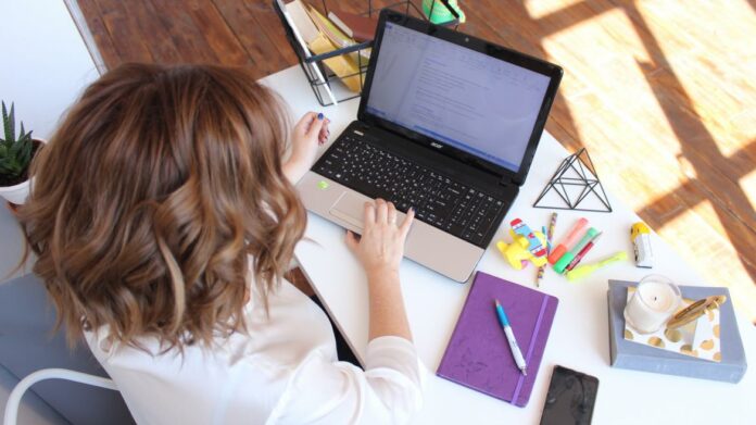 Mujer escribiendo en un ordenador sentada en una mesa con cosas de papeleria